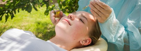 Cometologist massage therapist takes care of the skin of a girl in nature with natural cosmetics, oils for skin care, massage from natural ingredients, herbs, natural cosmetics